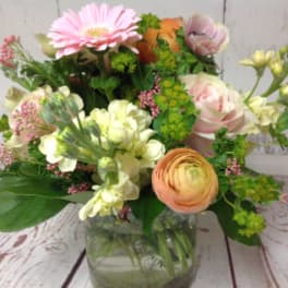 Mixed arrangement of pink, peach, and cream flowers in a clear glass vase on a wood surface