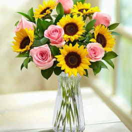 Pink roses and yellow sunflowers in a clear glass vase