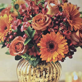 Orange roses and gerbera daisies in a gold vase