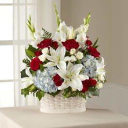 Tall red rose, white lily, and blue hydrangea basket arrangement in a white woven container