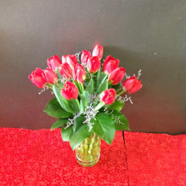 Red tulip arrangement in a yellow glass vase on a red patterned cloth