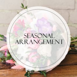 Round bouquet with pink, white, and lavender flowers wrapped in clear paper