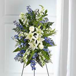Tall standing spray of white lilies and blue flowers arranged on a metal easel