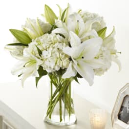 White lilies and hydrangeas arranged in a clear glass vase on a light-colored surface