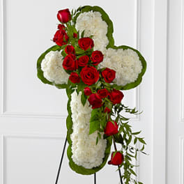 Cross-shaped floral tribute with red roses and white flowers on a stand