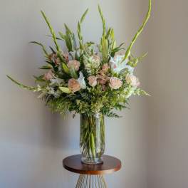 Tall bouquet of pale roses, white lilies, and greenery in a clear glass vase