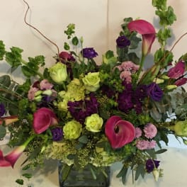 Large mixed bouquet with pink calla lilies, purple blooms, and green hydrangeas in a glass vase