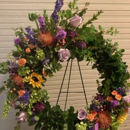 Large floral wreath on a black stand with purple, orange, and yellow blooms