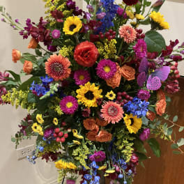 Large colorful standing floral arrangement with sunflowers, roses, and daisies