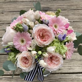 Bouquet of pink and white flowers in a clear vase with a striped ribbon