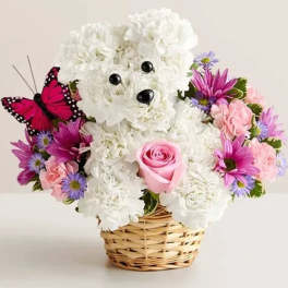Basket arrangement with a white carnation dog, pink rose, and purple daisies with a faux butterfly.