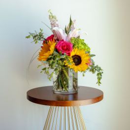 Mixed bouquet in a clear glass vase with sunflowers, roses, and lilies
