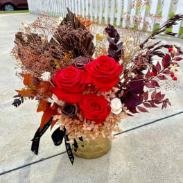 Red roses in a gold vase with dried foliage and berries