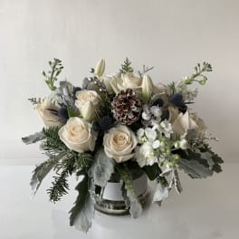 Cream roses and white lilies arranged in a glass vase with pinecone accents