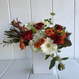 Mixed bouquet of red and orange roses with white daisies in a white vase