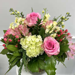 Compact arrangement of pink roses, hydrangea, and mixed pastel blooms in a clear glass vase