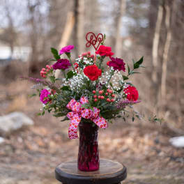 Pink and red carnation bouquet in a glass vase with a heart ribbon