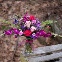 Mixed pink, purple, and red bouquet in a glass vase with a ribbon