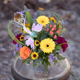 Mixed bouquet with yellow daisies, orange rose, and purple accents in a metal container