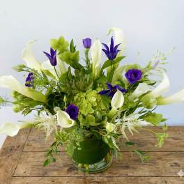 White calla lilies and purple flowers in a glass vase