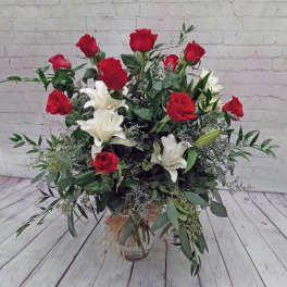 Tall arrangement of red roses and white lilies in a clear glass vase