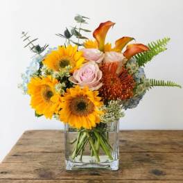 Bouquet of sunflowers, roses, and orange calla lilies in a glass vase