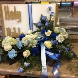 Religious floral tribute with white and blue flowers arranged before a Holy Bible plaque.