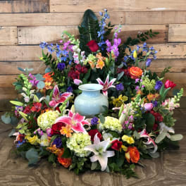 Colorful ring of mixed flowers surrounding a pale blue urn against a wood background