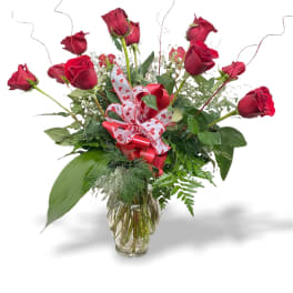 Red roses arranged in a clear glass vase with a heart ribbon