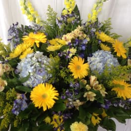 Basket arrangement of yellow daisies, blue hydrangeas, and purple flowers