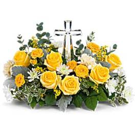 Yellow roses and white flowers arranged around a clear glass cross