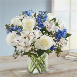 White roses and blue flowers in a clear glass vase