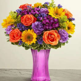 Colorful bouquet of roses, sunflowers, and purple flowers in a pink vase