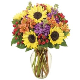 Bouquet of sunflowers, purple flowers, and orange blooms in a glass vase
