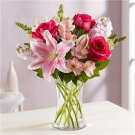Pink roses and lilies arranged in a clear glass vase