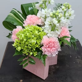 Pink and white floral arrangement in a pink box with green accents