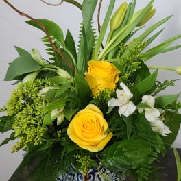 Yellow roses and white flowers in a patterned square vase