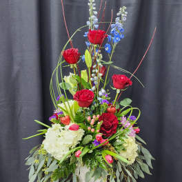 Tall floral arrangement with red roses, blue delphinium, and white hydrangeas