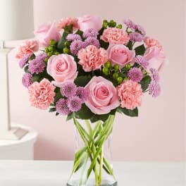Pink roses, carnations, and purple mums in a clear glass vase