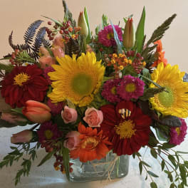 Mixed bouquet of sunflowers, roses, and gerbera daisies in a glass vase