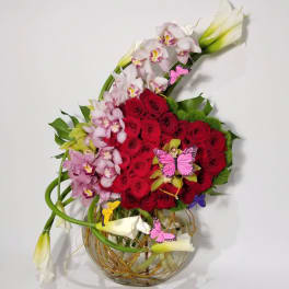 Red roses and pink orchids in a glass vase with butterfly picks