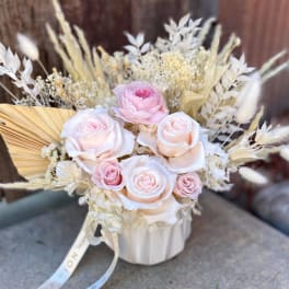 Pink and white roses arranged in a white vase with dried grasses