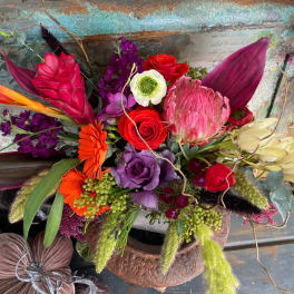 Colorful mixed bouquet with roses, protea, and orchids in a rustic container