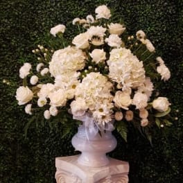 White floral arrangement in a white urn on a pedestal