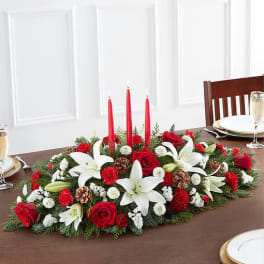 Holiday centerpiece with red candles, white lilies, and red roses on a table