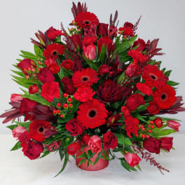 Large red floral arrangement with roses and gerbera daisies in a low vase