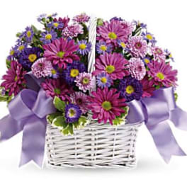 Purple and pink daisy bouquet in a white basket with lavender ribbon