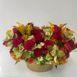 Mixed bouquet of red roses, green orchids, and orange flowers in a gold bowl