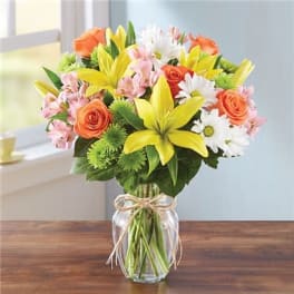 Bouquet of yellow lilies, orange roses, and white daisies in a glass vase