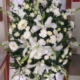 Large white funeral spray with lilies, daisies, and roses on an easel